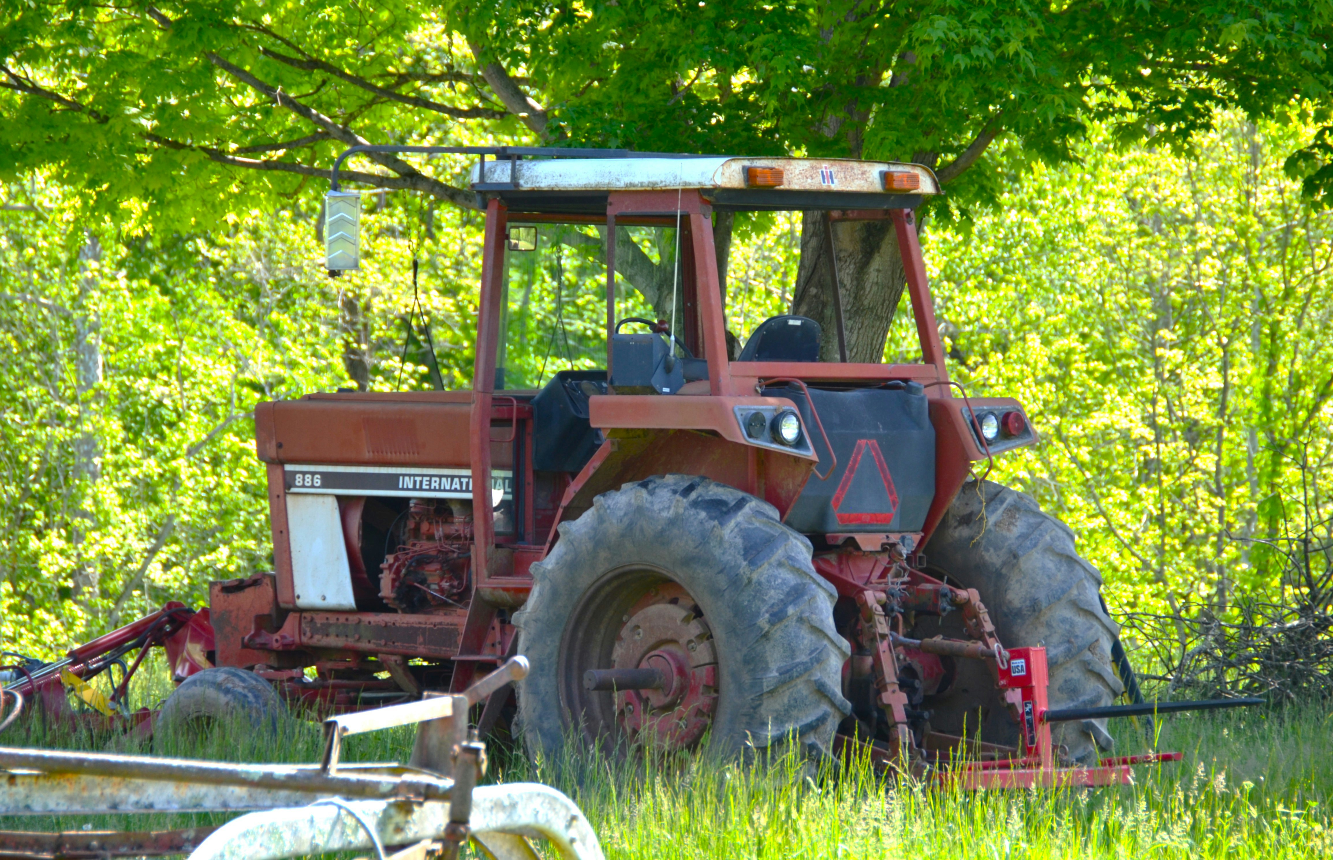 A rusty tractor parked under a tree